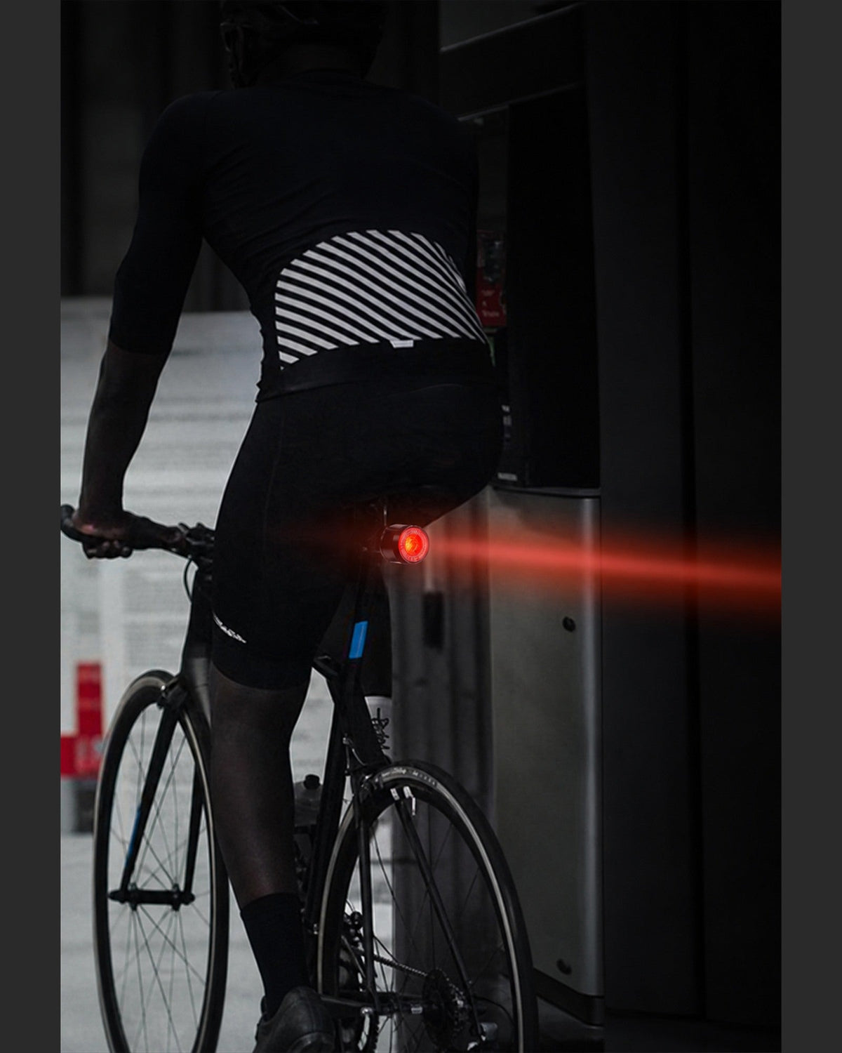 Cyclist viewed from behind with a red rear light beam extending across the road