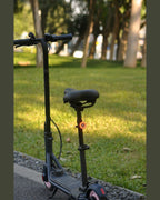 Parked scooter with a small red rear light beside a tree in a daylight scene