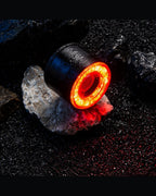 Round RGB halo bike light glowing red on wet rocks in a dark outdoor scene