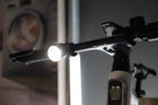 Handlebar-mounted bike light shining a bright white beam in a close-up scene
